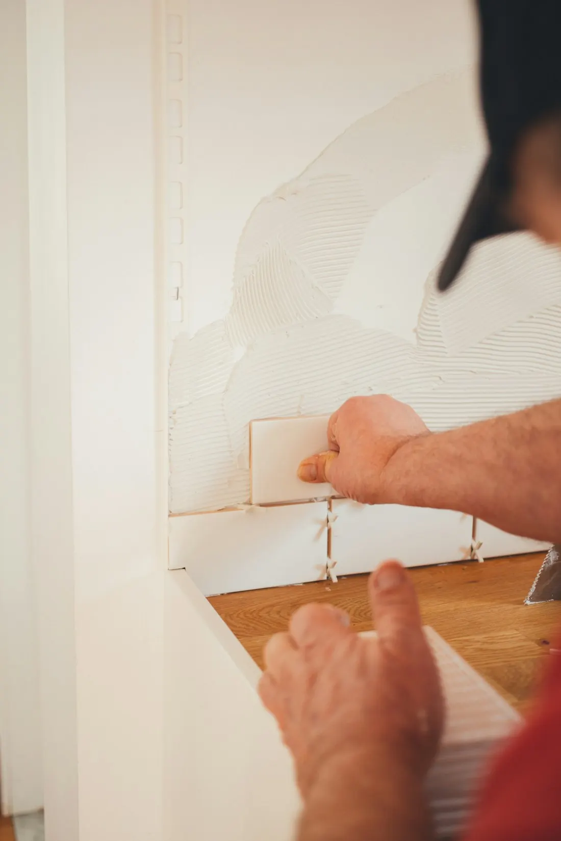 Hands pressing a white tile into fresh thinset